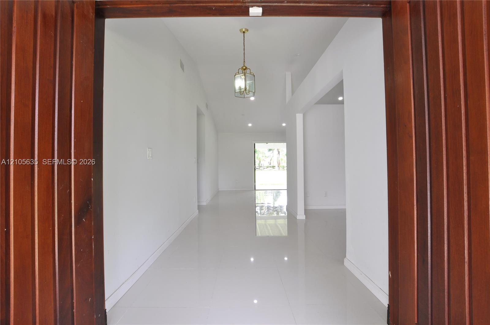 Entryway featuring vertical wood-paneled door trim, high ceilings, polished tile flooring, and a decorative pendant light fixture