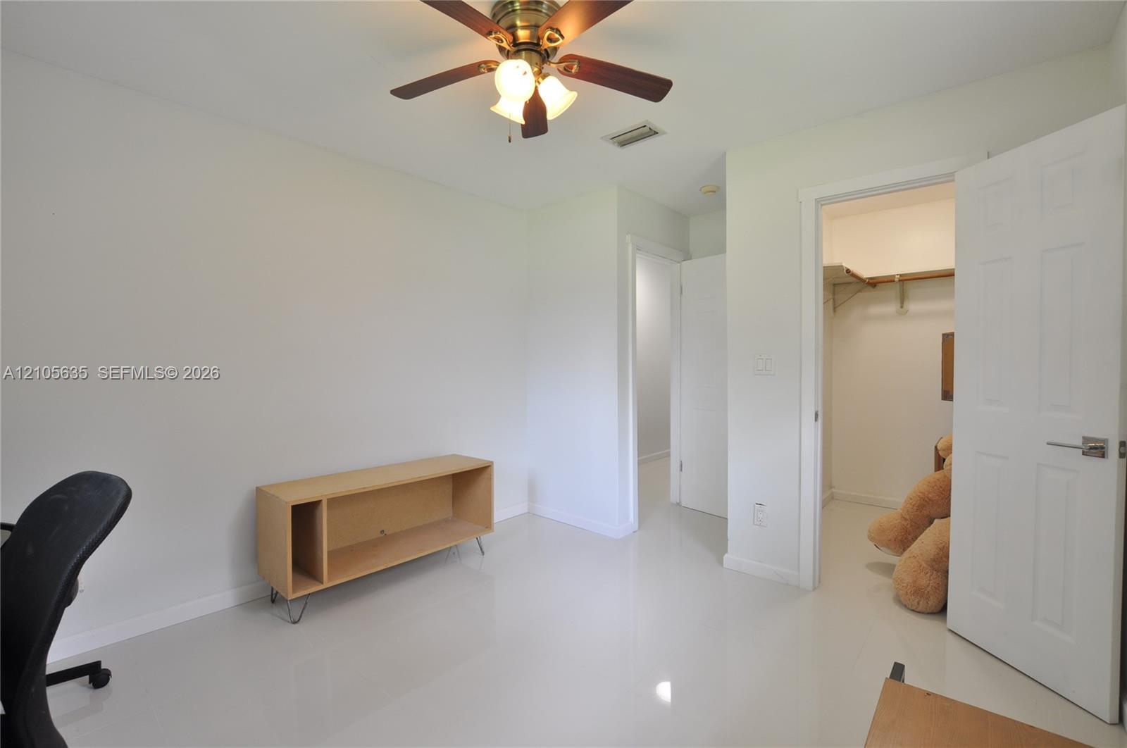 Room featuring glossy tile flooring, a six-panel door, walk-in closet with built-in shelving, and a ceiling fan with integrated lighting