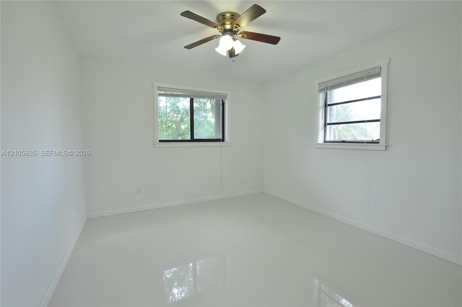 Neutral-toned interior space featuring light-colored tile flooring, two windows with horizontal blinds, and a multi-blade ceiling fan with integrated lighting