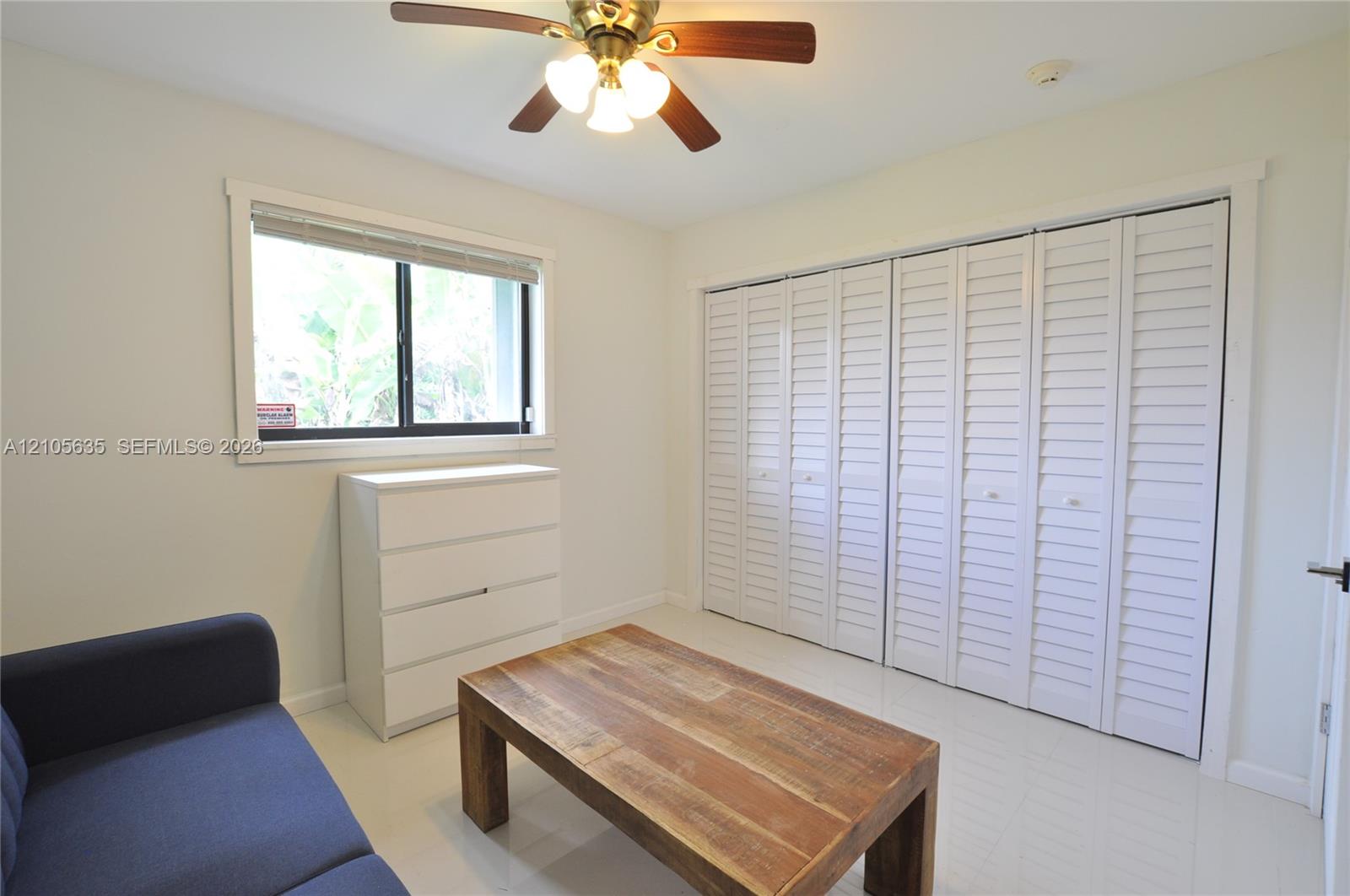 Room featuring white shutter-style closet doors, a ceiling fan with integrated lighting, a dual-pane window, and high-gloss tile flooring