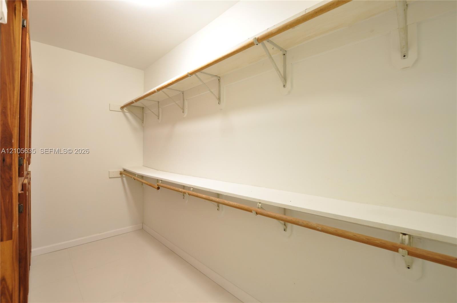 Storage space featuring tiered shelving, integrated wooden hanging rods, and neutral flooring