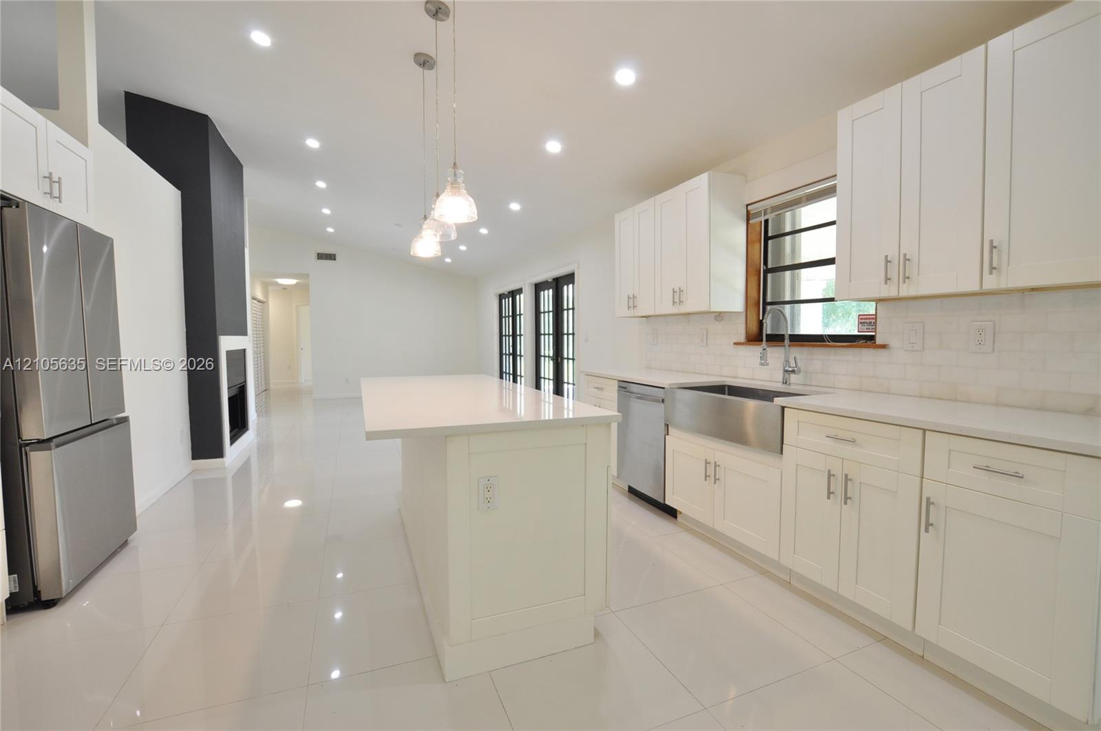 Kitchen featuring white shaker-style cabinetry, quartz countertops, a stainless steel apron-front sink, an island with pendant lighting, and polished tile flooring
