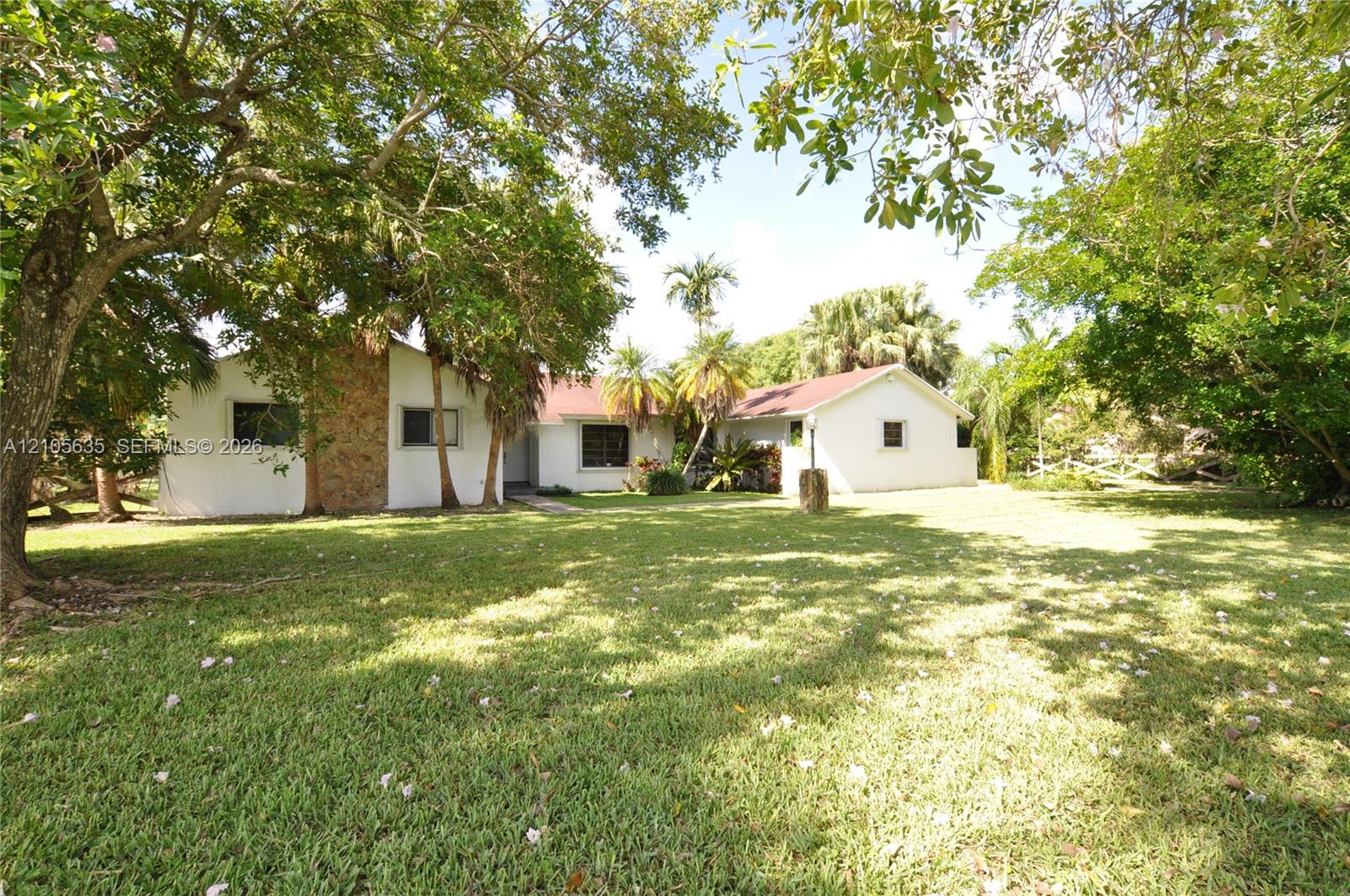 Expansive grounds featuring mature shade trees, a stone-accented facade, and a low-pitched roofline