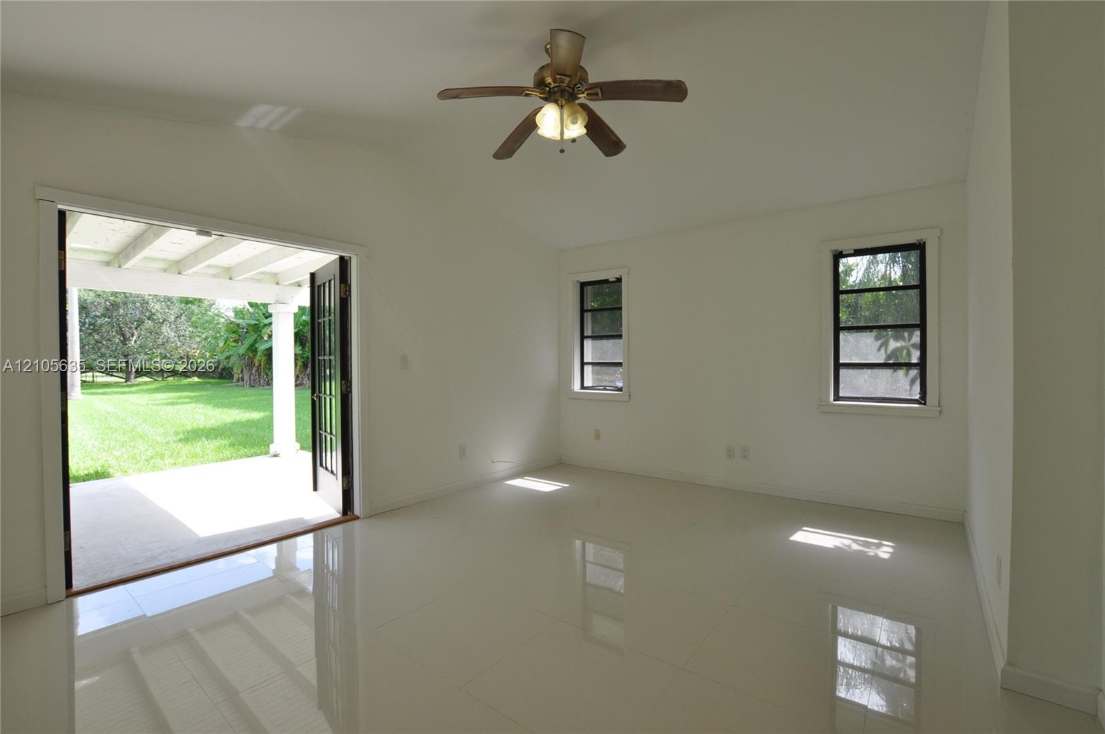 Room featuring large-format tile flooring, vaulted ceilings, a central ceiling fan, and black-framed double doors opening to a covered patio