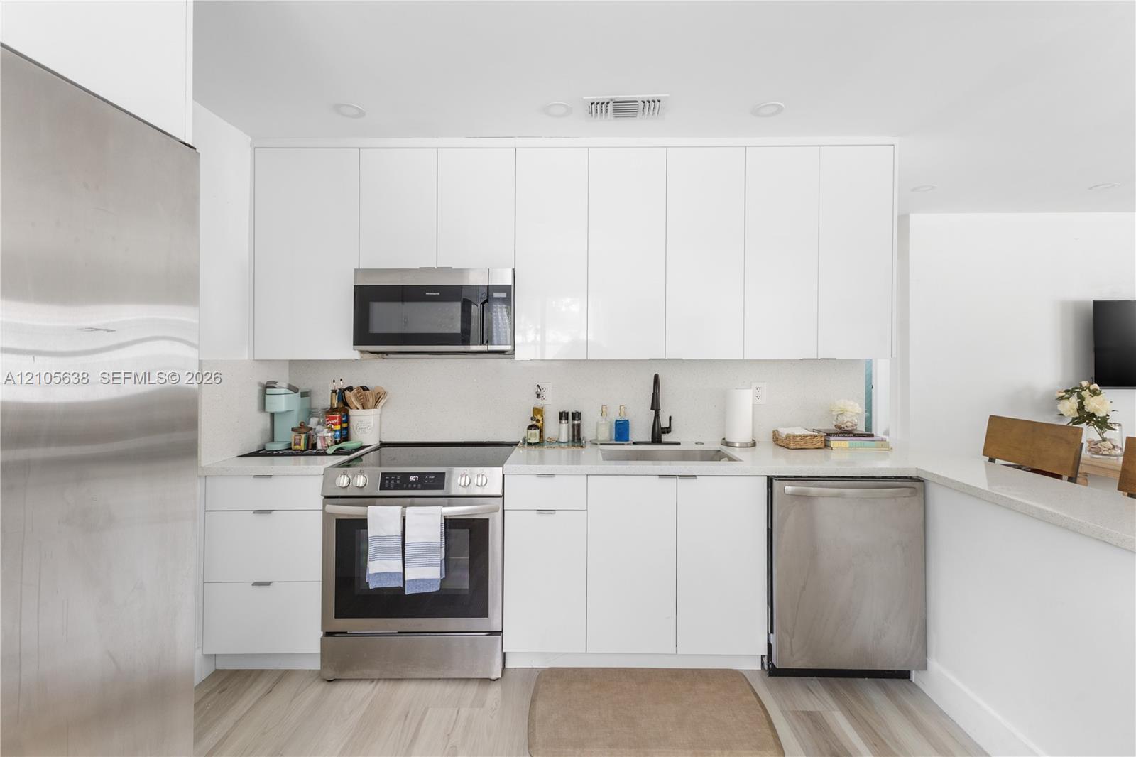 Kitchen featuring flat-panel white cabinetry, stone-finish countertops, stainless steel appliances, matte black faucet, and wood-finish flooring