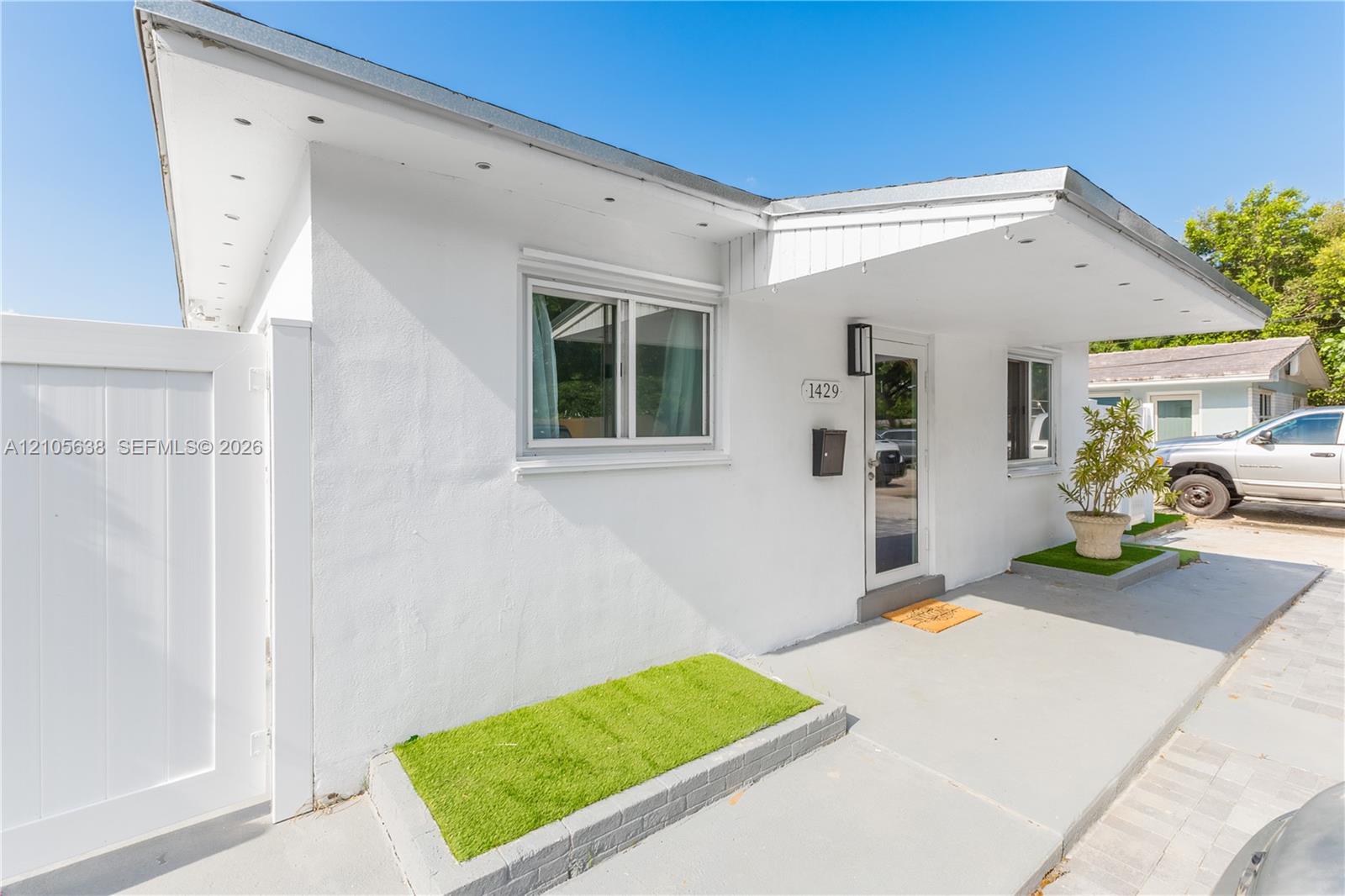 Exterior featuring smooth white stucco finish, extended roof overhang with integrated lighting, dual-pane windows, and a dedicated concrete porch area with built-in planter beds