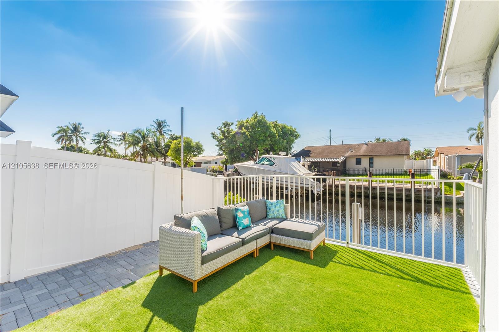 Waterfront patio featuring synthetic turf, interlocking paver hardscaping, and a white privacy fence with aluminum perimeter railing