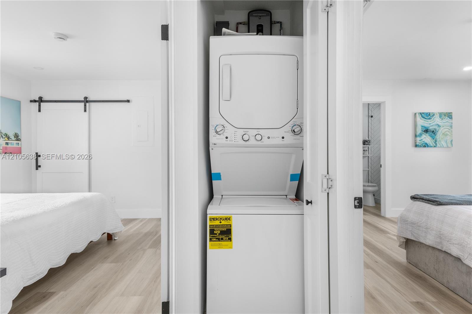 Built-in stacked laundry unit with bi-fold closet doors, white walls, and wood-finish flooring
