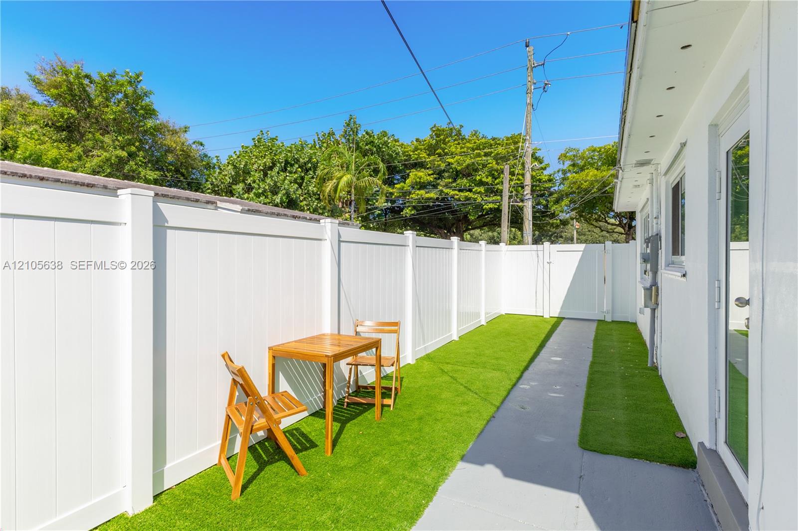 Exterior side patio featuring synthetic turf, concrete walkway, and white vinyl privacy fencing