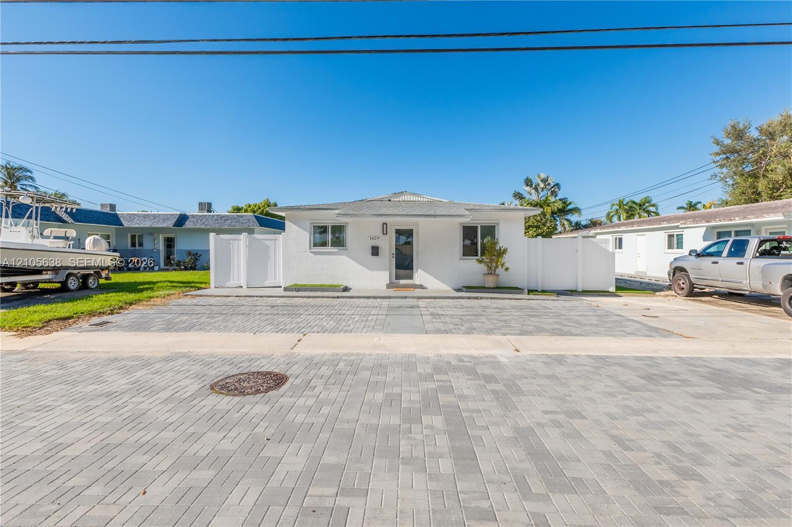 Single-story exterior featuring white stucco siding, a paved brick driveway, and integrated white privacy fencing