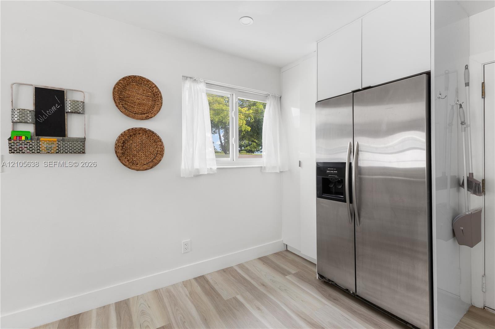 Stainless steel side-by-side refrigerator, white full-height cabinetry, and wood-finish flooring