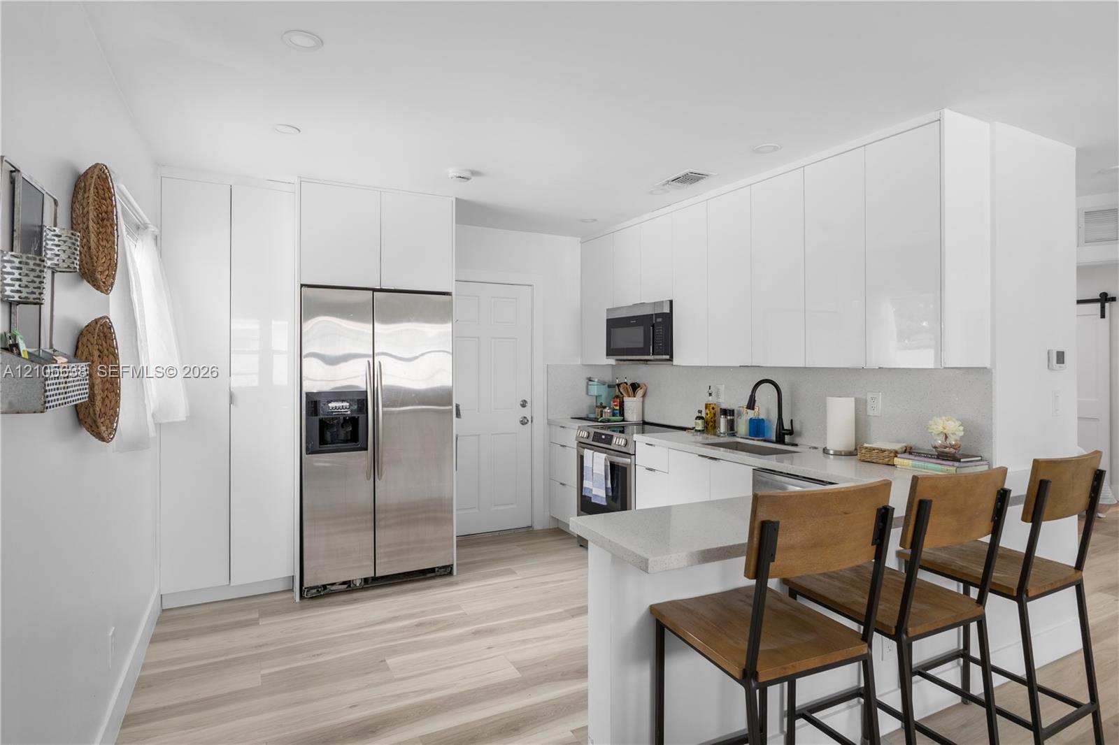 Kitchen featuring white flat-panel cabinetry, stainless steel appliances, quartz countertops, a matte black faucet, and wood-finish flooring