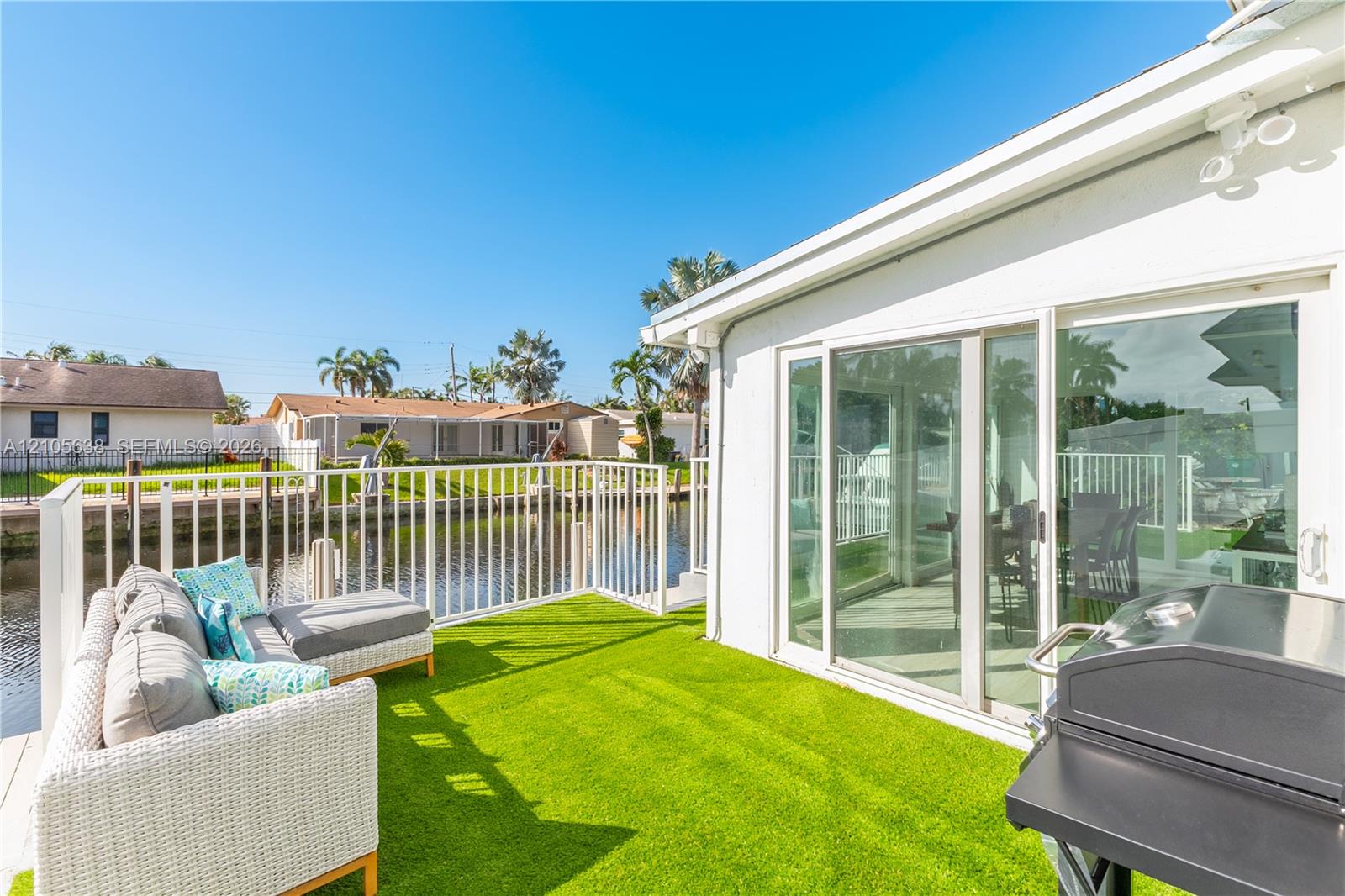 Waterfront patio featuring synthetic turf surfacing, white metal perimeter railings, and sliding glass door access
