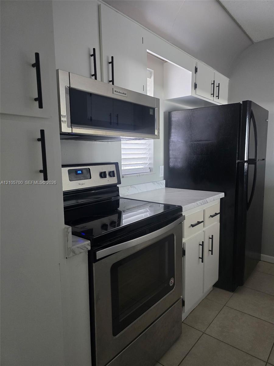 Kitchen featuring white cabinetry with matte black hardware, stone-finish countertops, stainless steel oven and microwave, and large-format tile flooring Kitchen featuring white cabinetry with matte black hardware, stone-finish countertops, stainless steel oven and microwave, and large-format tile flooring