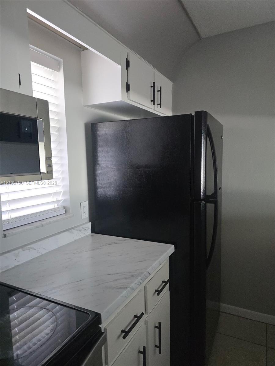 White cabinetry featuring matte black hardware, stone-patterned countertops, and integrated stainless steel and black appliances White cabinetry featuring matte black hardware, stone-patterned countertops, and integrated stainless steel and black appliances