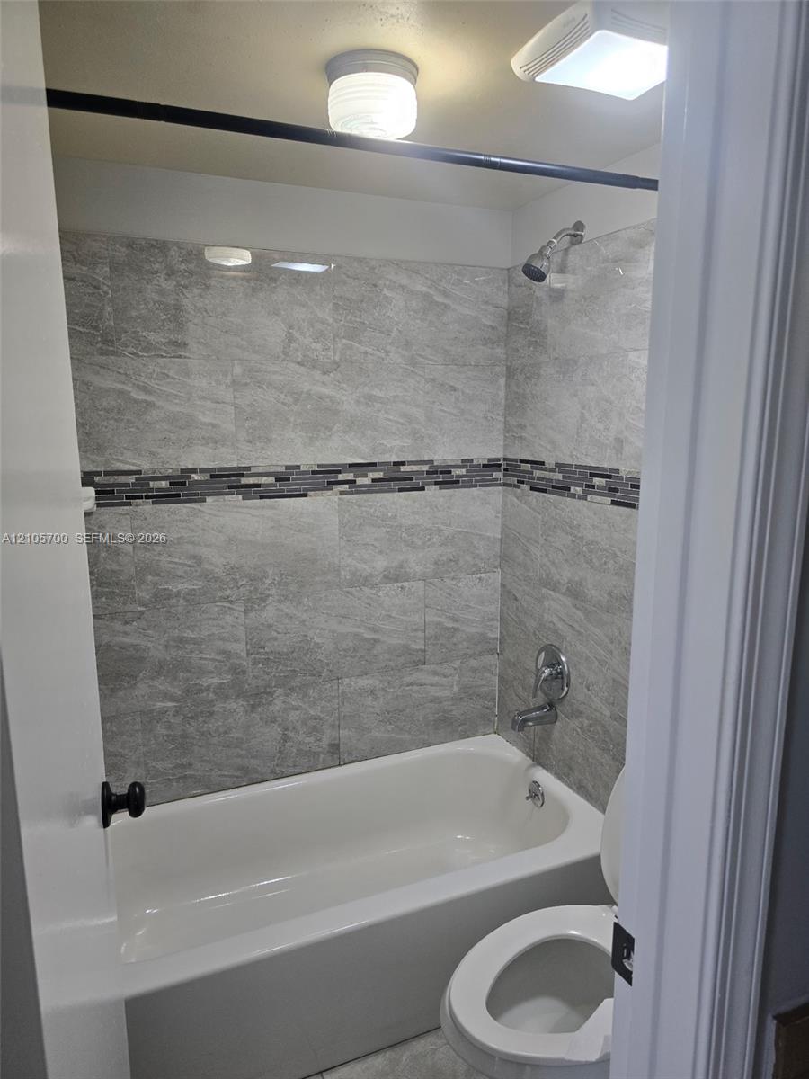 Bathtub surround featuring large-format grey tile, mosaic accent detailing, polished chrome fixtures, and a ceiling-mounted light fixture Bathtub surround featuring large-format grey tile, mosaic accent detailing, polished chrome fixtures, and a ceiling-mounted light fixture