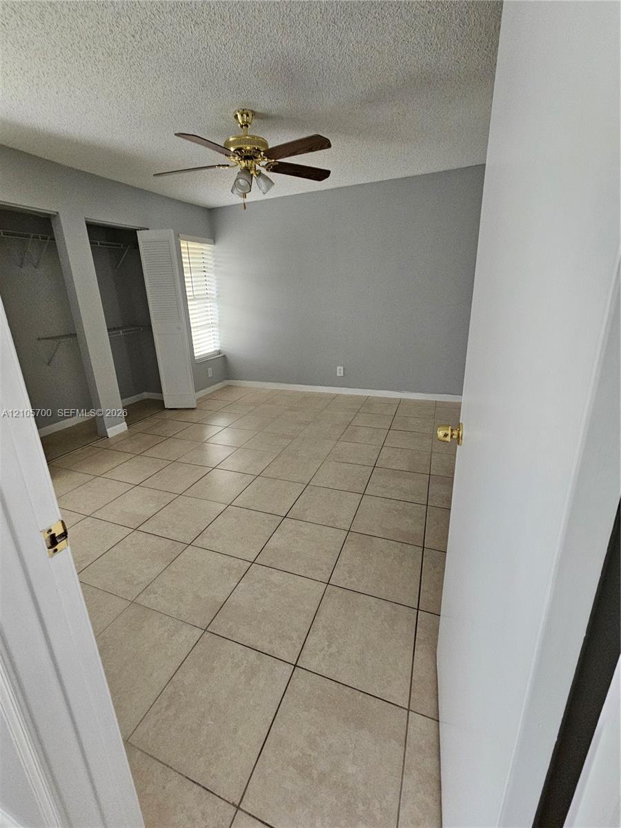 Room interior featuring large-format ceramic tile flooring, neutral wall paint, dual closets with louvered doors, and a ceiling fan with integrated lighting