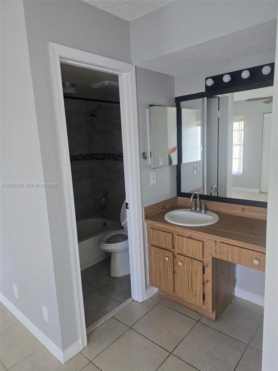 Bathroom featuring wood-finish cabinetry, an integrated vanity surface, a wall-mounted mirror with matte black trim, and ceramic tile flooring