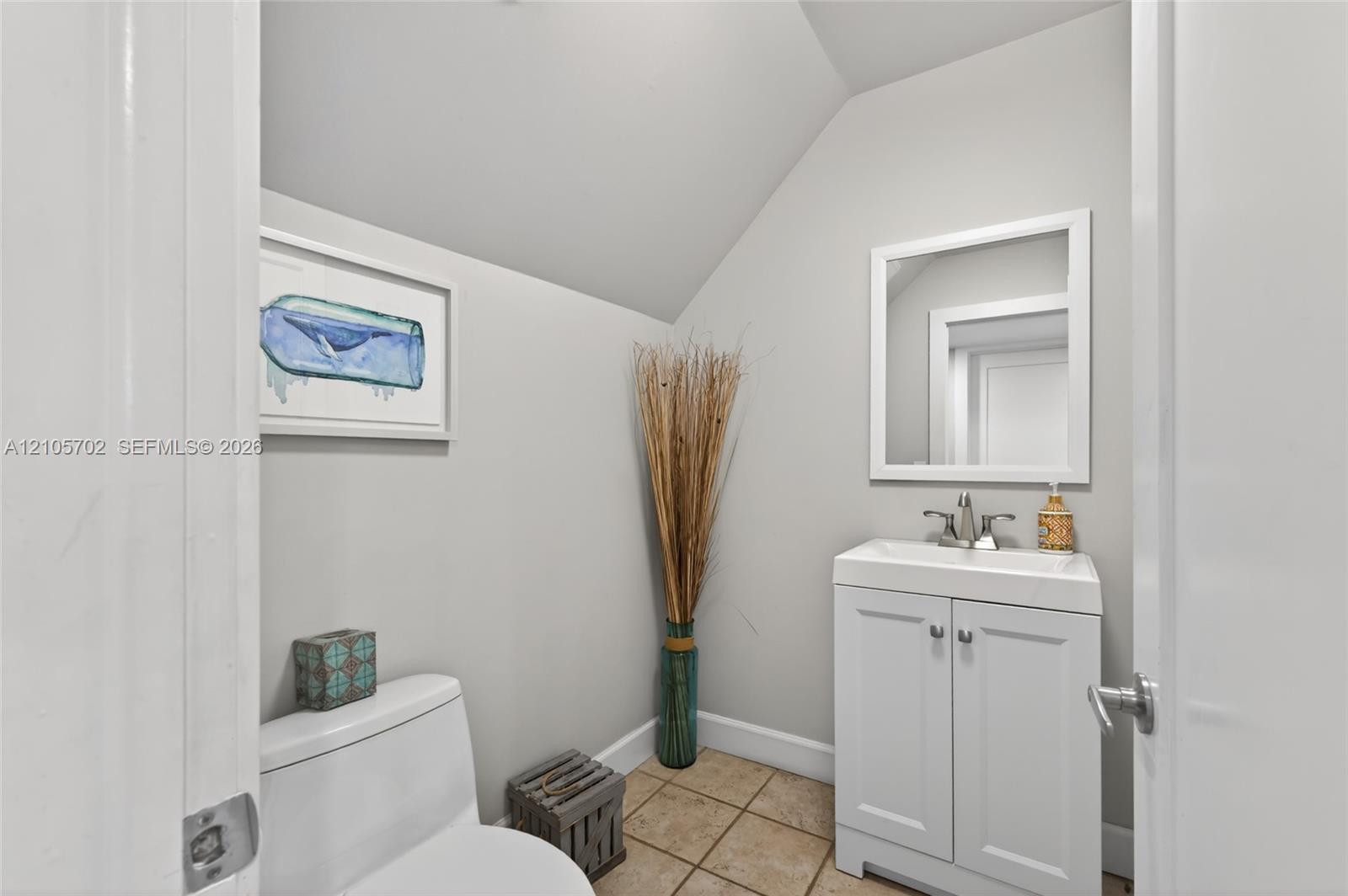 White vanity cabinet featuring a rectangular basin, chrome faucet, and rectangular wall-mounted mirror, complemented by tile flooring and neutral wall paint