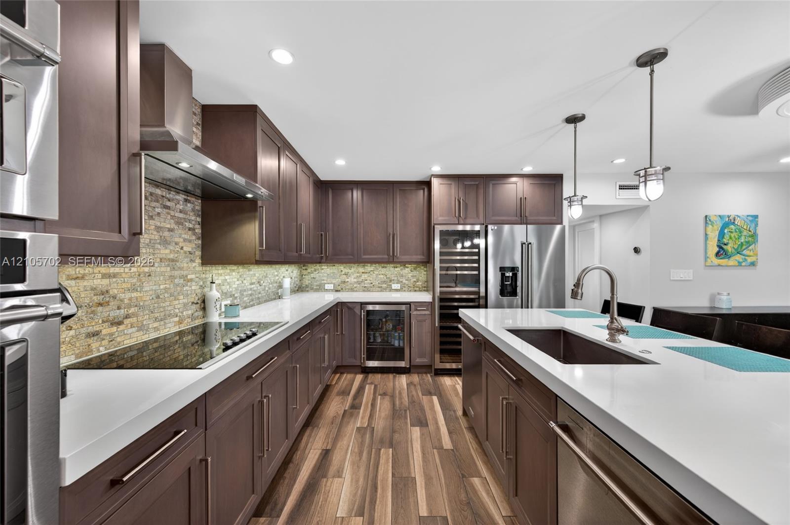Kitchen featuring dark-finish cabinetry, white countertops, stacked-stone backsplash, integrated stainless steel appliances including a wine refrigerator, and wood-finish flooring