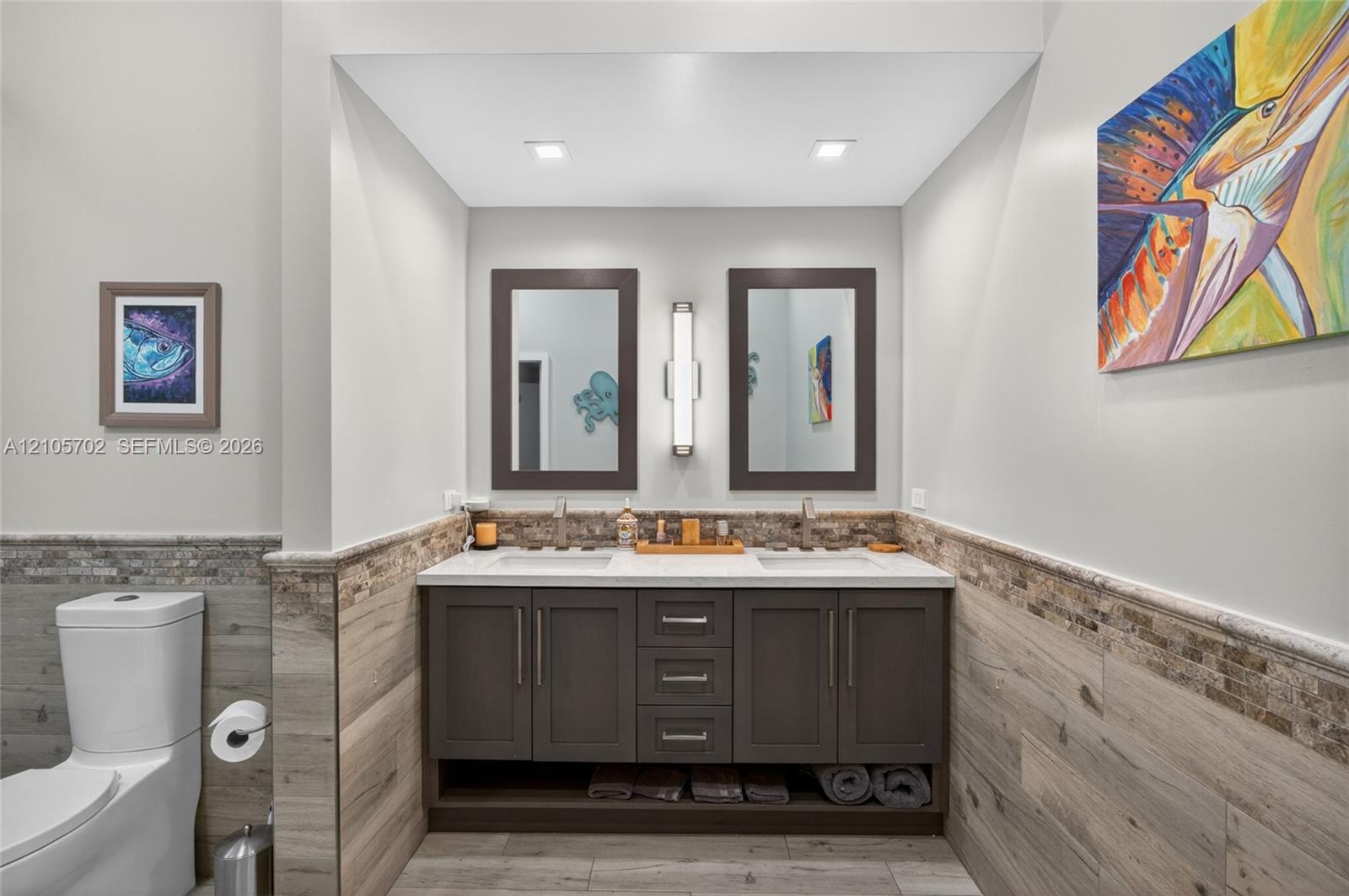 Double vanity featuring dark cabinetry, light-toned solid surface countertop, two undermount sinks, and a stone-tile backsplash