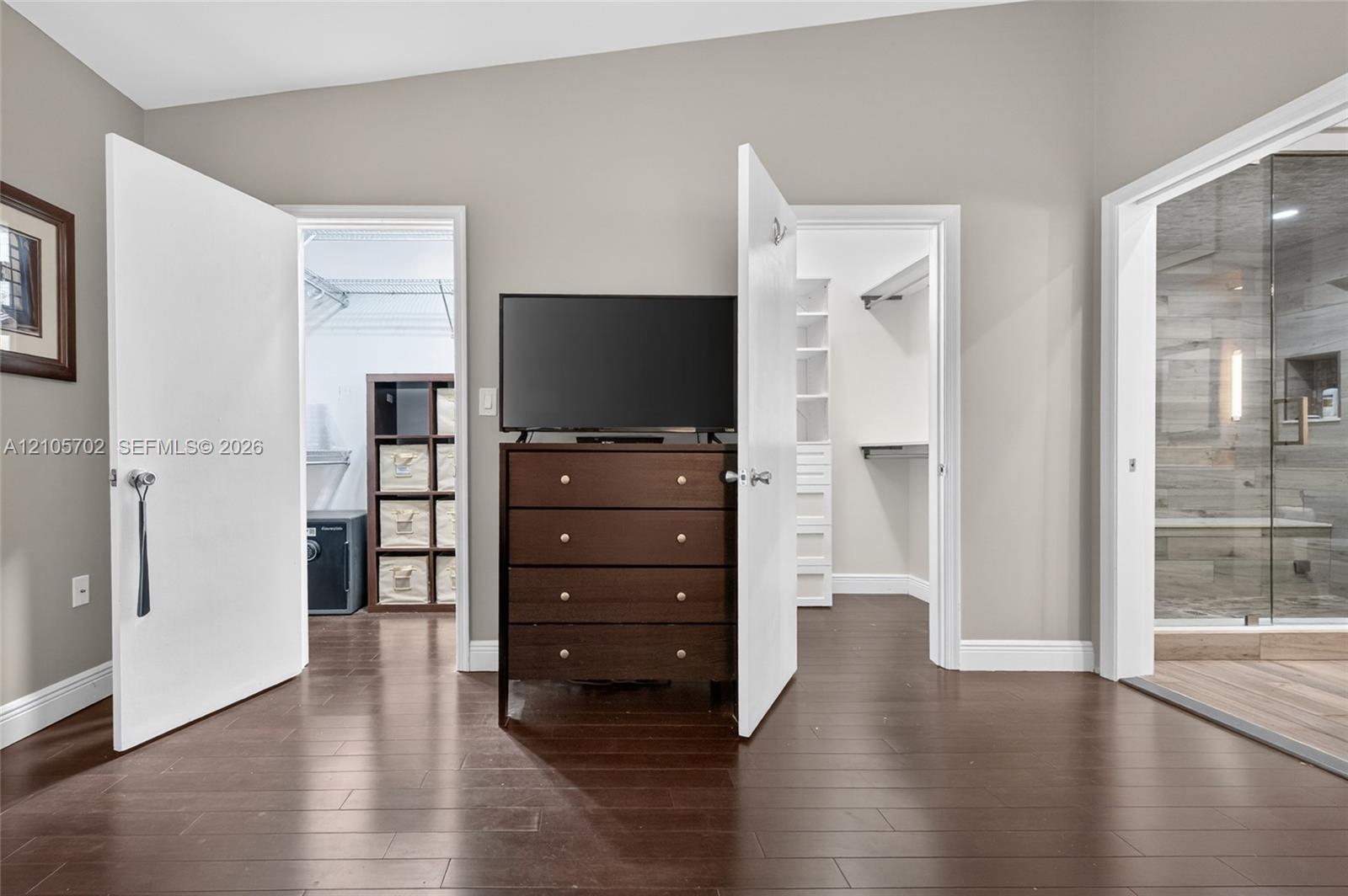 Room featuring wood-finish flooring, two walk-in closets with built-in shelving, and a glass-enclosed shower with tiled walls