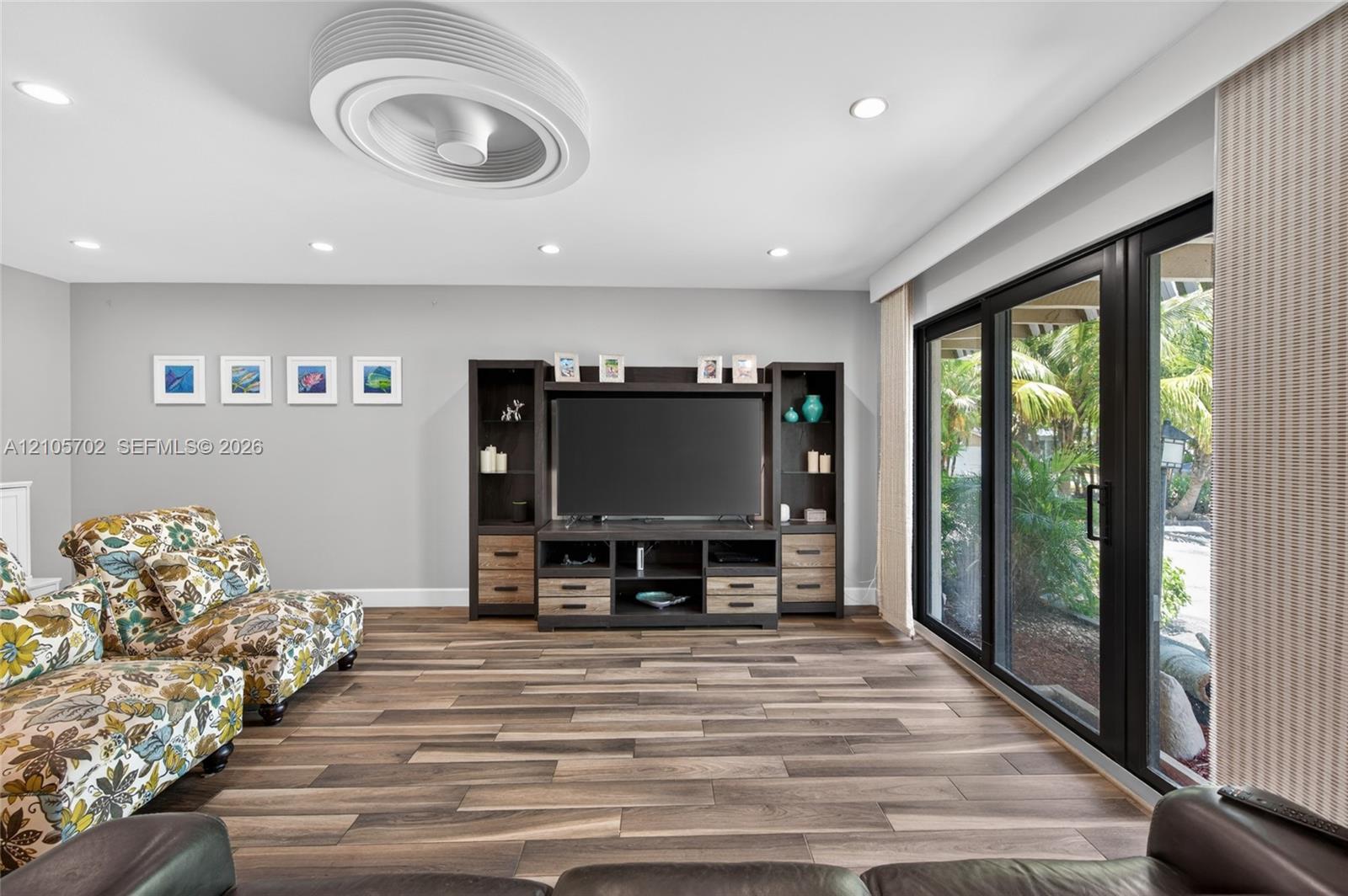 Living space featuring wood-finish flooring, recessed lighting, a modern circular ceiling fan, a built-in media console, and large sliding glass doors