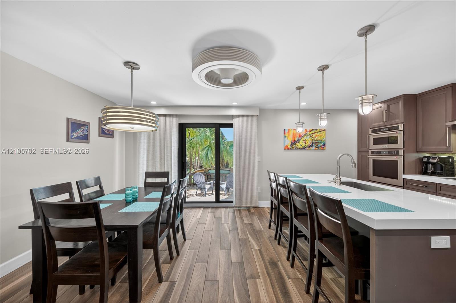 Kitchen featuring wood-finish flooring, quartz-topped center island with a stainless steel sink, built-in double wall ovens, and custom cabinetry