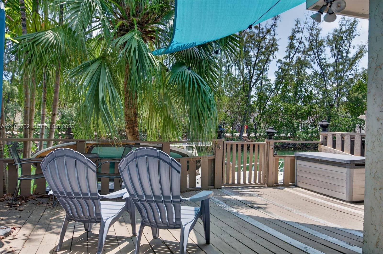 Wood-plank deck featuring a wooden perimeter railing with a gate, mature palm trees, and canal-side positioning