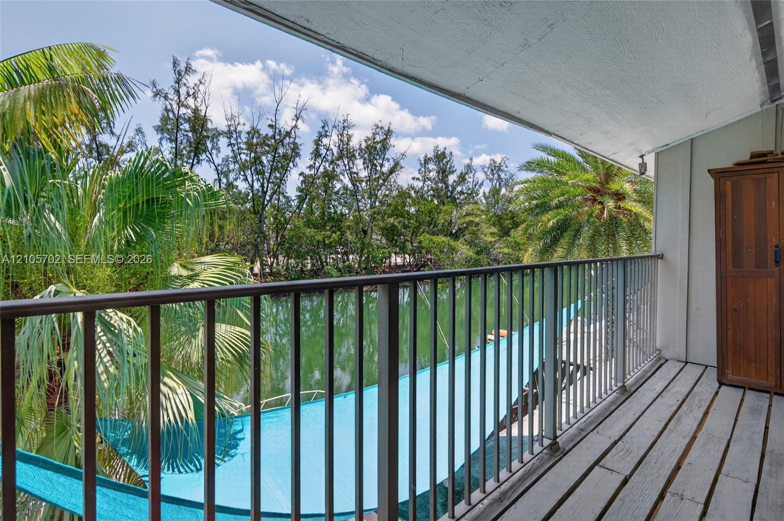 Covered balcony featuring metal railings, slatted flooring, and built-in storage cabinetry, overlooking a waterway with mature palm trees