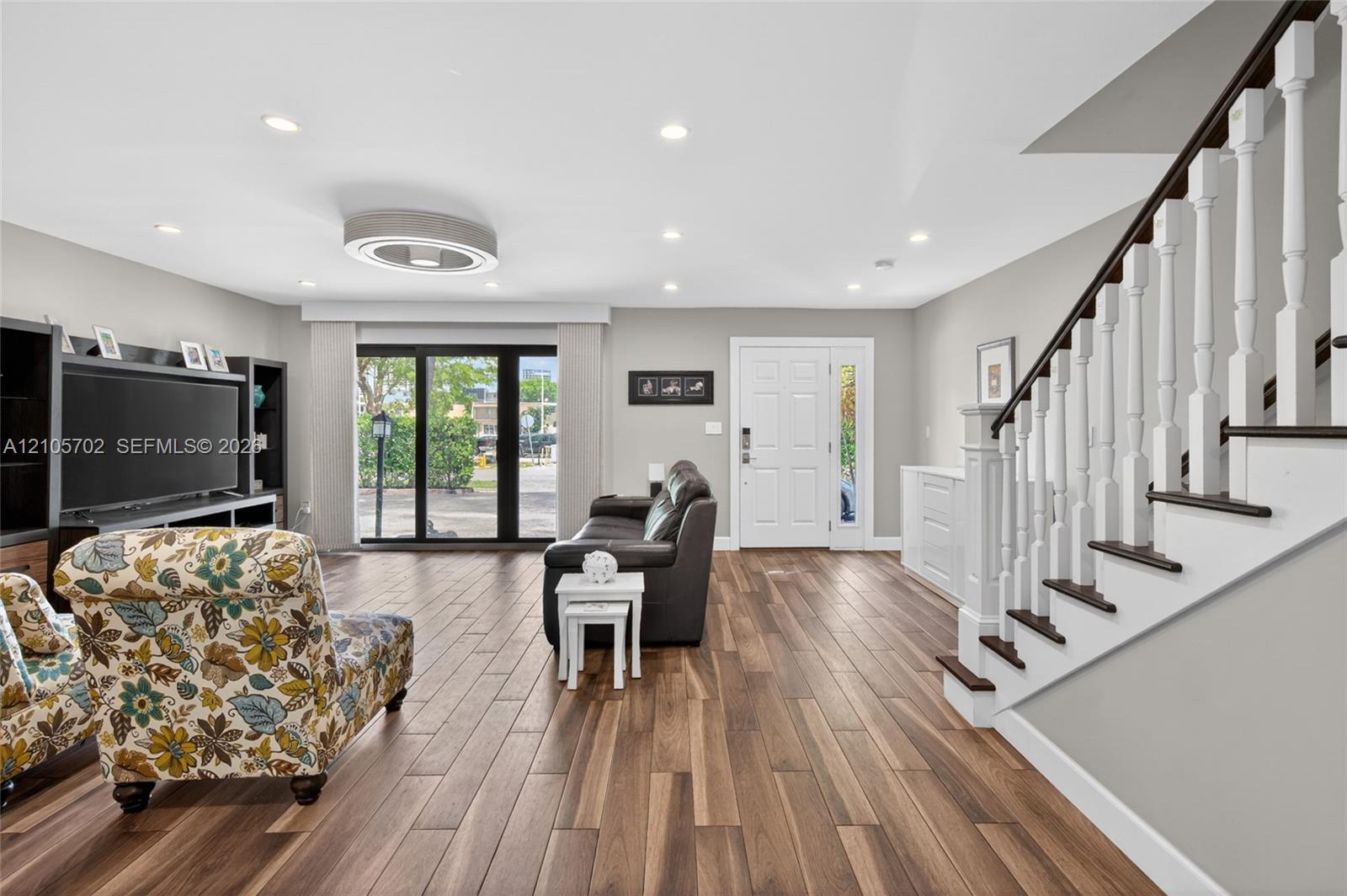 Open living space featuring wood-finish flooring, recessed lighting, built-in cabinetry, and a staircase with a white balustrade and dark wood handrail