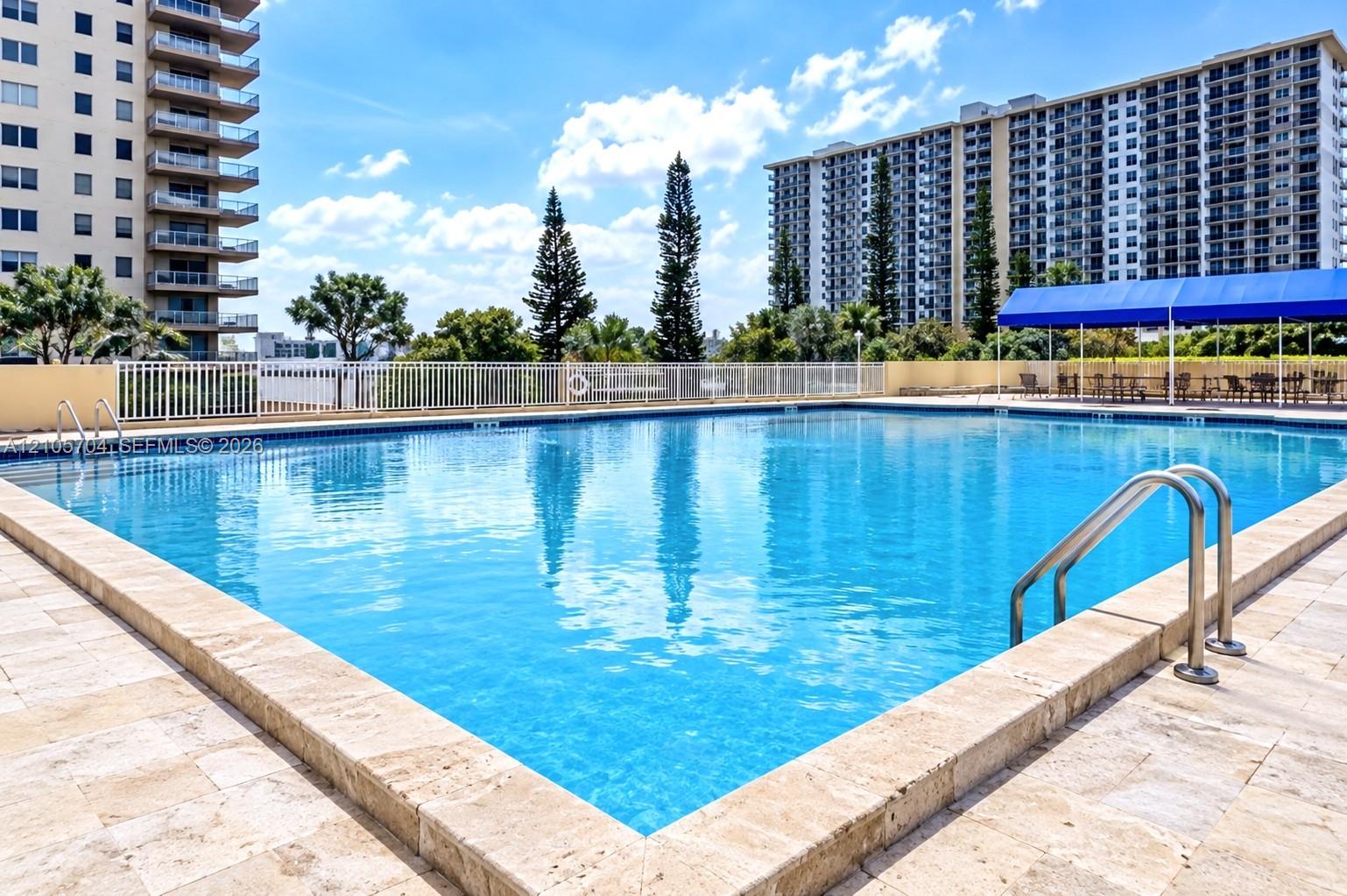 Rectangular swimming pool featuring a natural stone deck, metal pool ladders, and a blue canopy structure