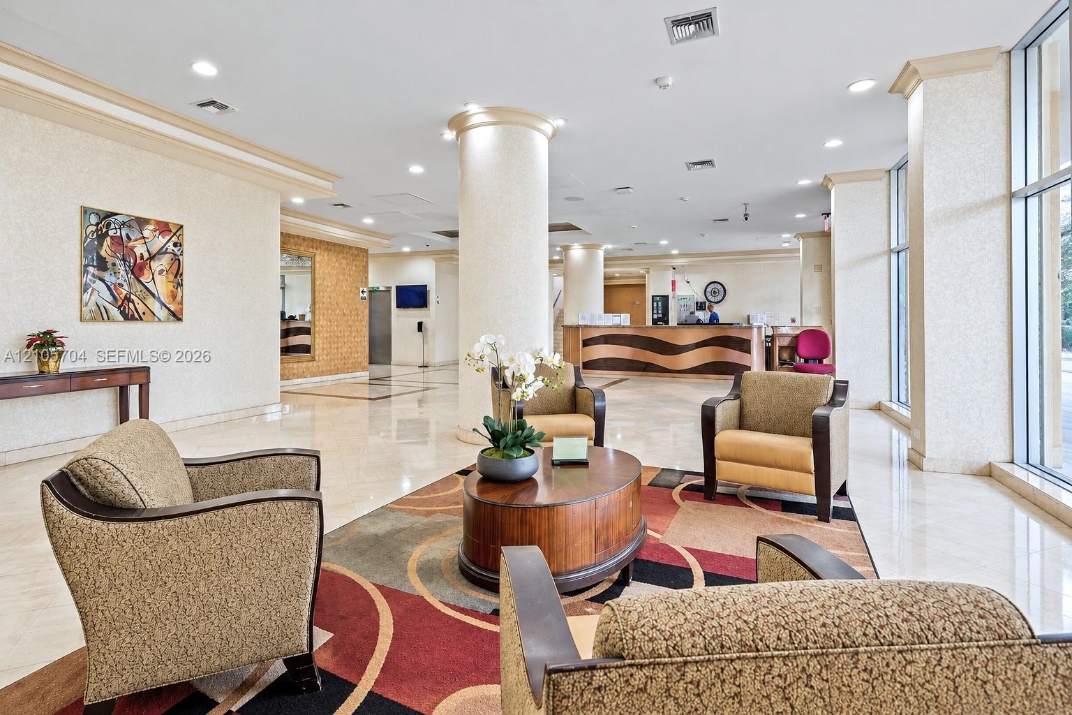 Lobby featuring polished stone flooring, floor-to-ceiling windows, structural columns, and a custom built-in reception desk with curved millwork