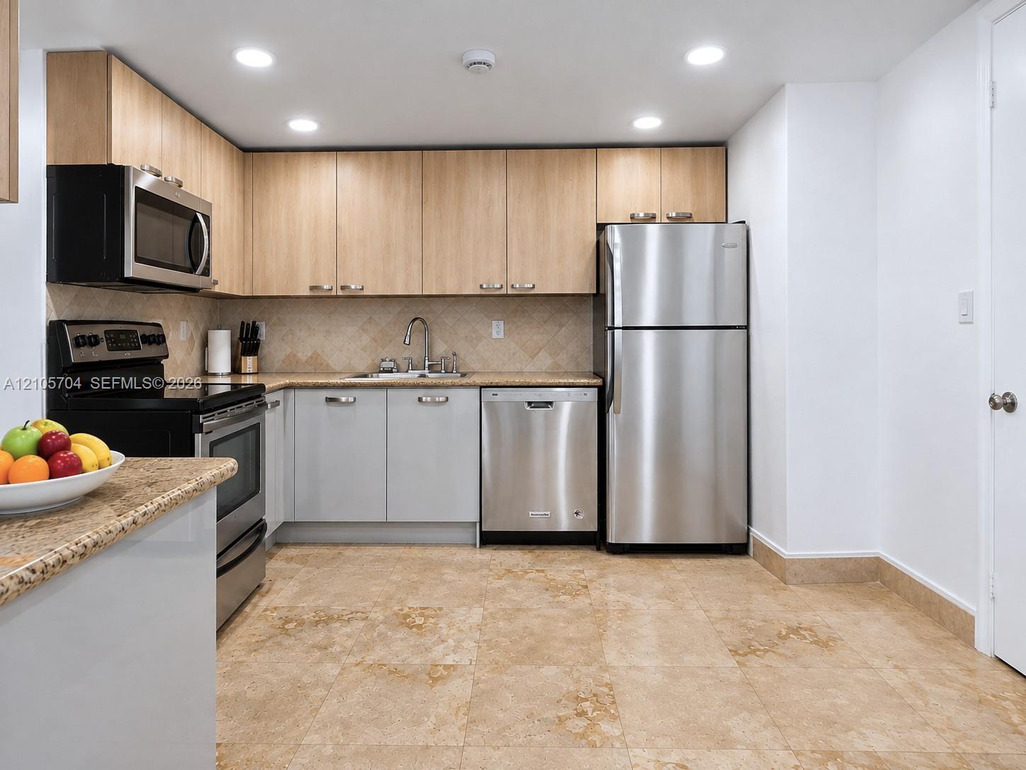 Kitchen featuring two-tone cabinetry, stainless steel appliances, speckled stone-finish countertops, tiled backsplash, and stone-finish flooring
