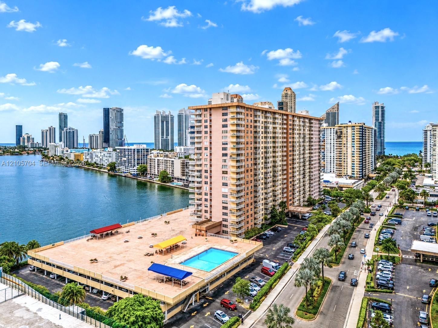 High-rise residential building featuring a waterfront location, an elevated outdoor swimming pool, a parking structure, and extensive surrounding cityscape