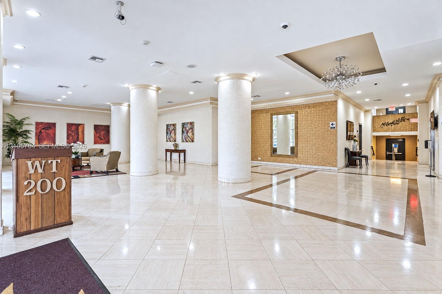 Grand lobby featuring polished stone tile flooring with decorative inlay, structural architectural columns, recessed tray ceilings, and a decorative sunburst chandelier