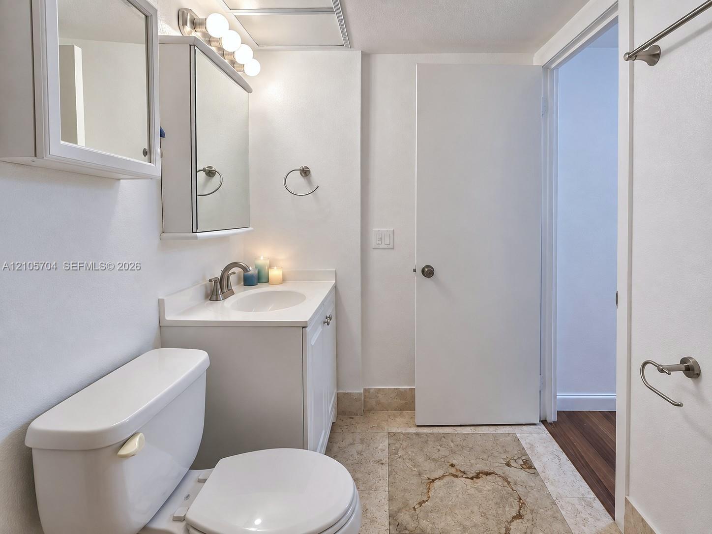 Bathroom featuring a vanity with a white countertop and integrated sink, mirrored medicine cabinet, brushed nickel-finish hardware, and stone-tile flooring