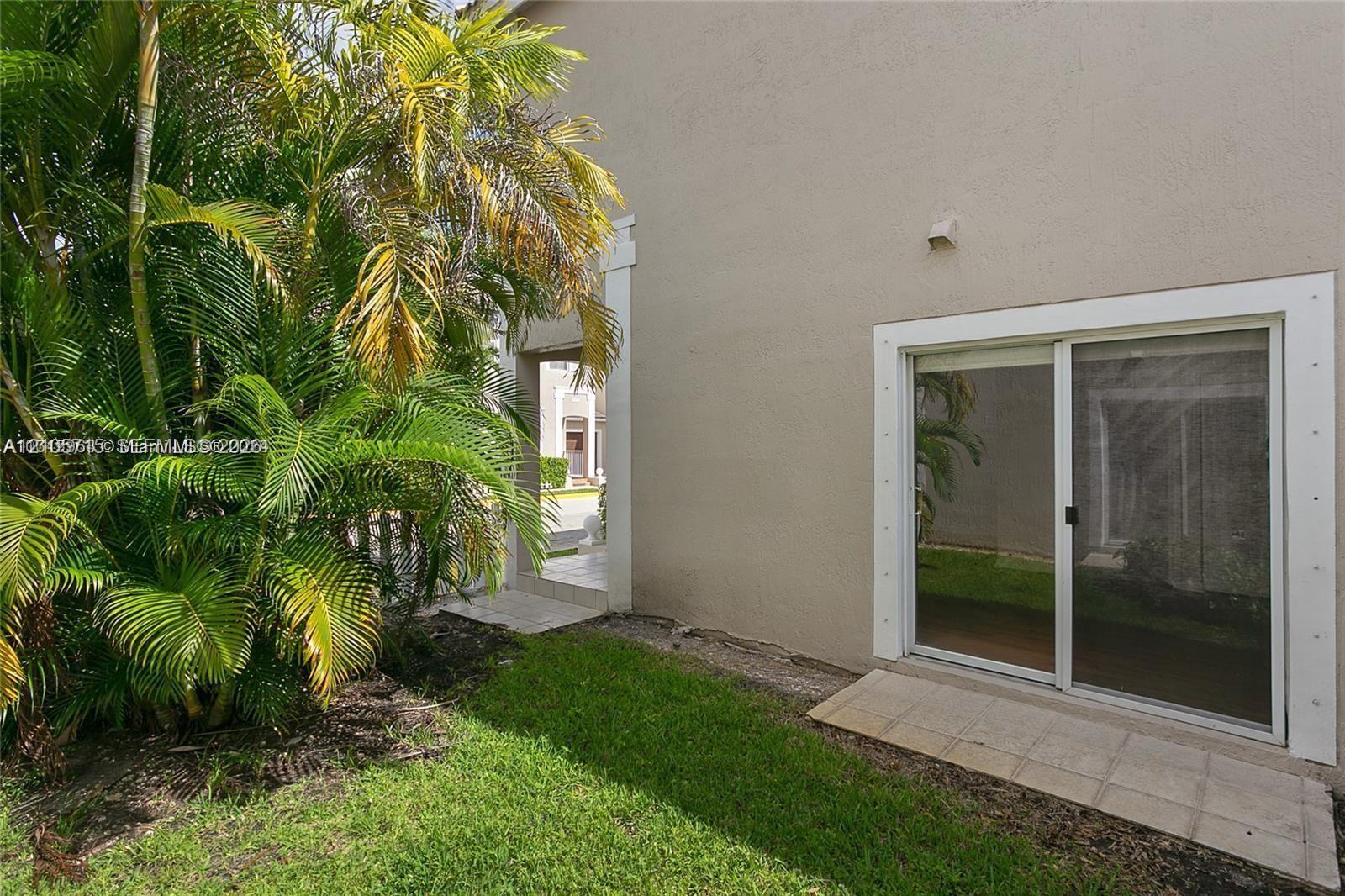 Stucco exterior featuring sliding glass doors with white trim, tile patio landing, and established palm landscaping