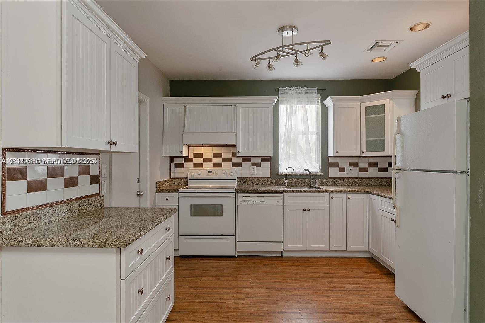 Kitchen featuring white cabinetry, stone-finish countertops, geometric tile backsplash, wood-finish flooring, and integrated lighting fixtures