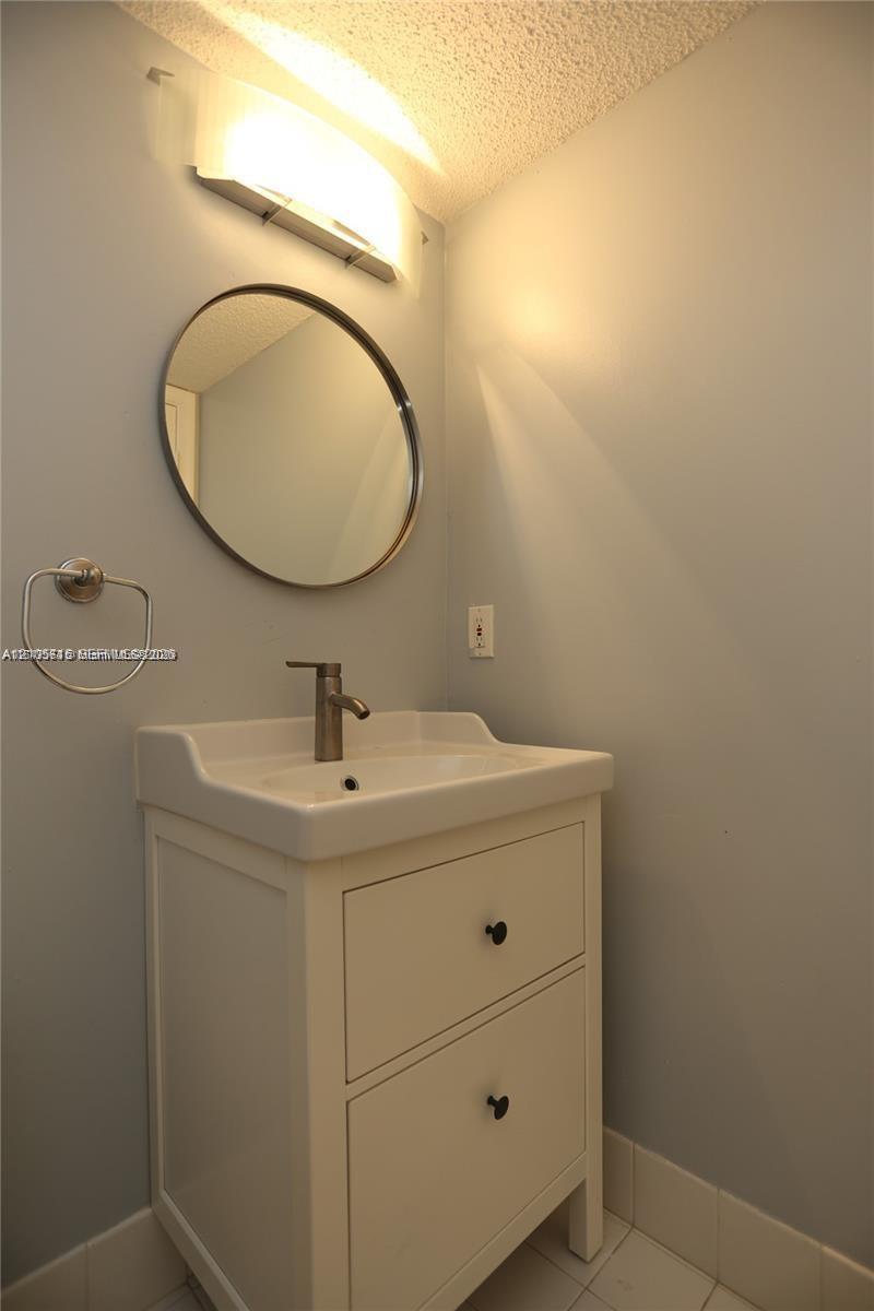 White vanity with two drawers, integrated porcelain basin, metallic finish faucet, round mirror, and wall-mounted light fixture