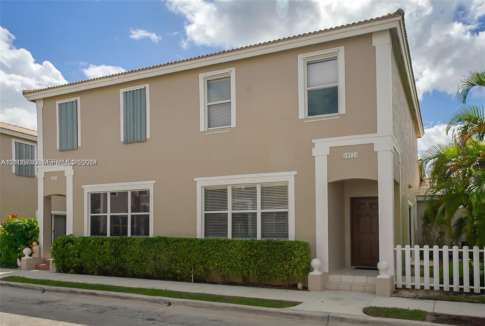 Two-story stucco exterior featuring a hipped tile roof, defined architectural trim, hurricane shutters, and a white picket fence Two-story stucco exterior featuring a hipped tile roof, defined architectural trim, hurricane shutters, and a white picket fence