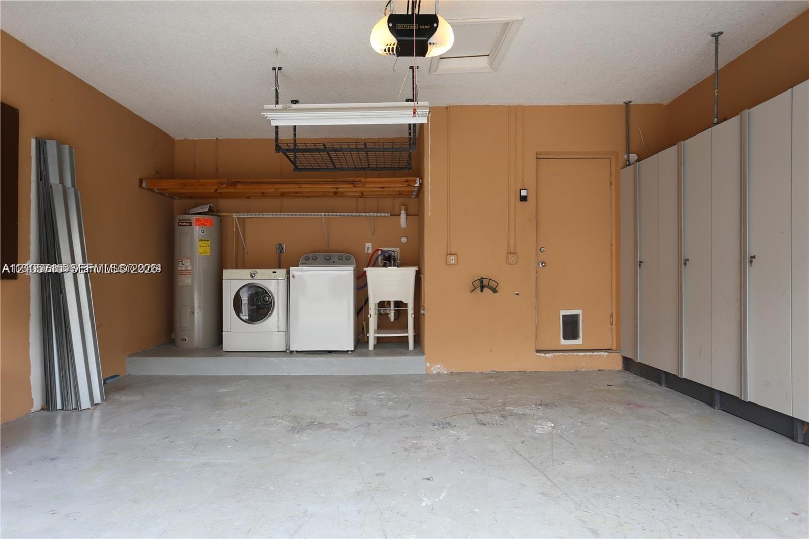 Garage space featuring built-in floor-to-ceiling cabinetry, overhead ceiling storage rack, utility sink, and wall-mounted shelving