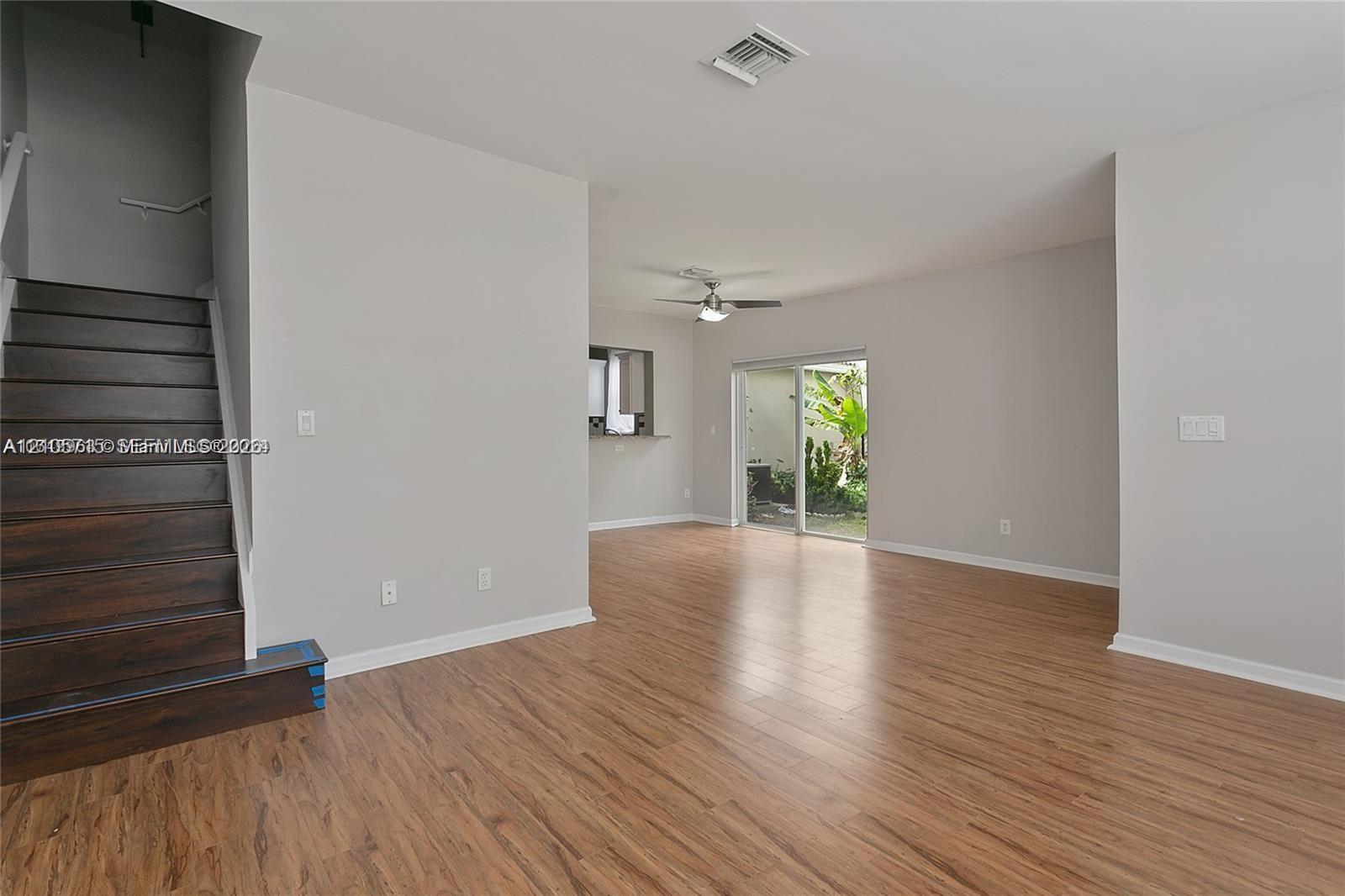 Open interior featuring wood-finish flooring, a staircase with dark wood-finish treads, a neutral wall palette, a ceiling-mounted fan, and glass sliding doors