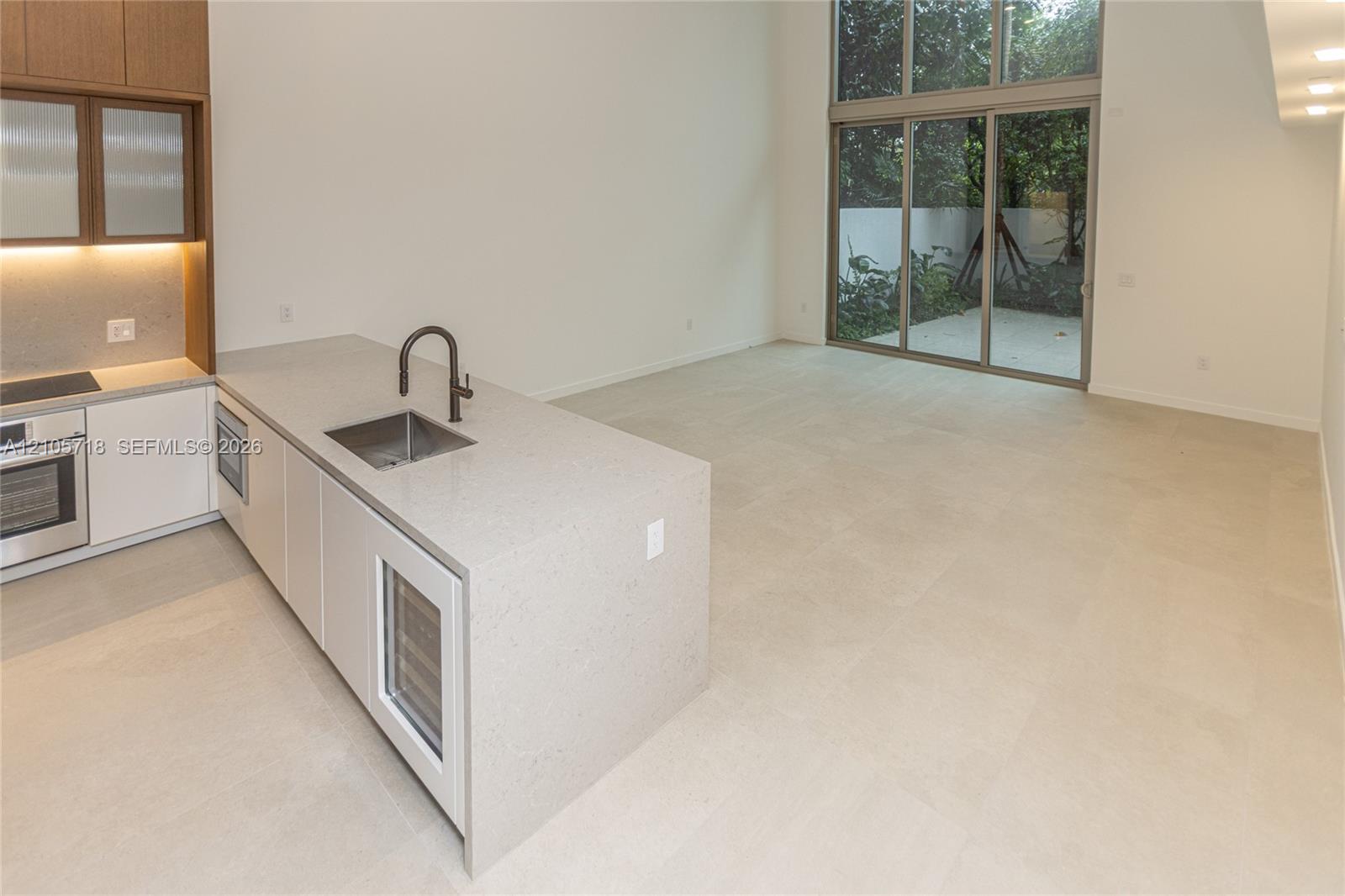 Kitchen featuring a stone-surface island, built-in wine refrigeration, high-ceiling glass sliding doors, and large-format tile flooring