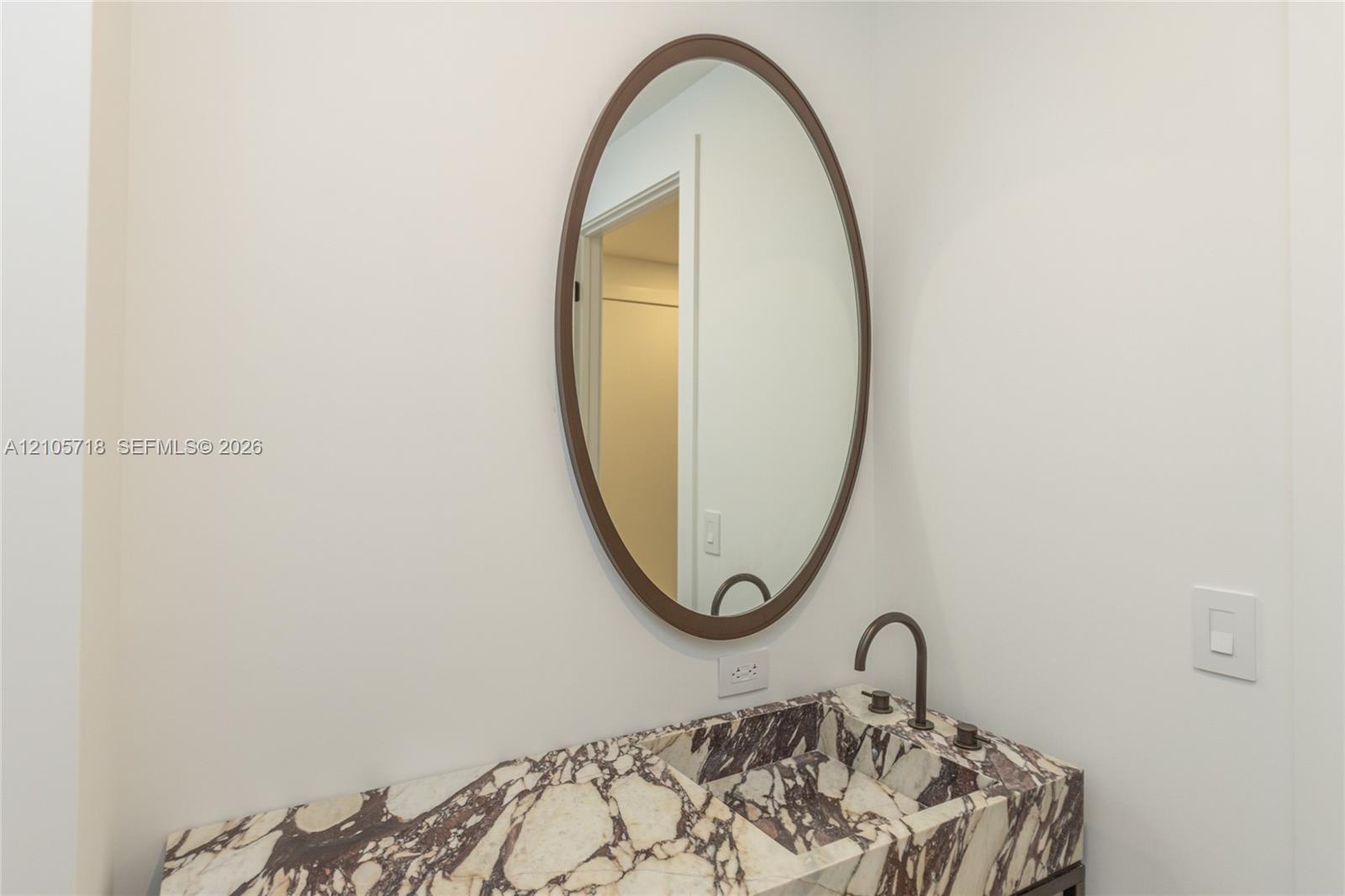 Stone countertop with an integrated basin, oval wall-mounted mirror with a bronze-toned frame, and a bronze-toned gooseneck faucet