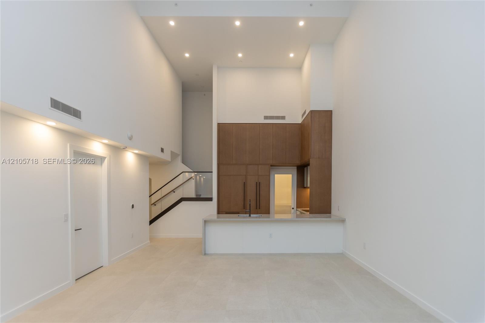 Double-height ceilings featuring recessed lighting, full-height wood-finish cabinetry, stone-surfaced kitchen island, and metal railing staircase