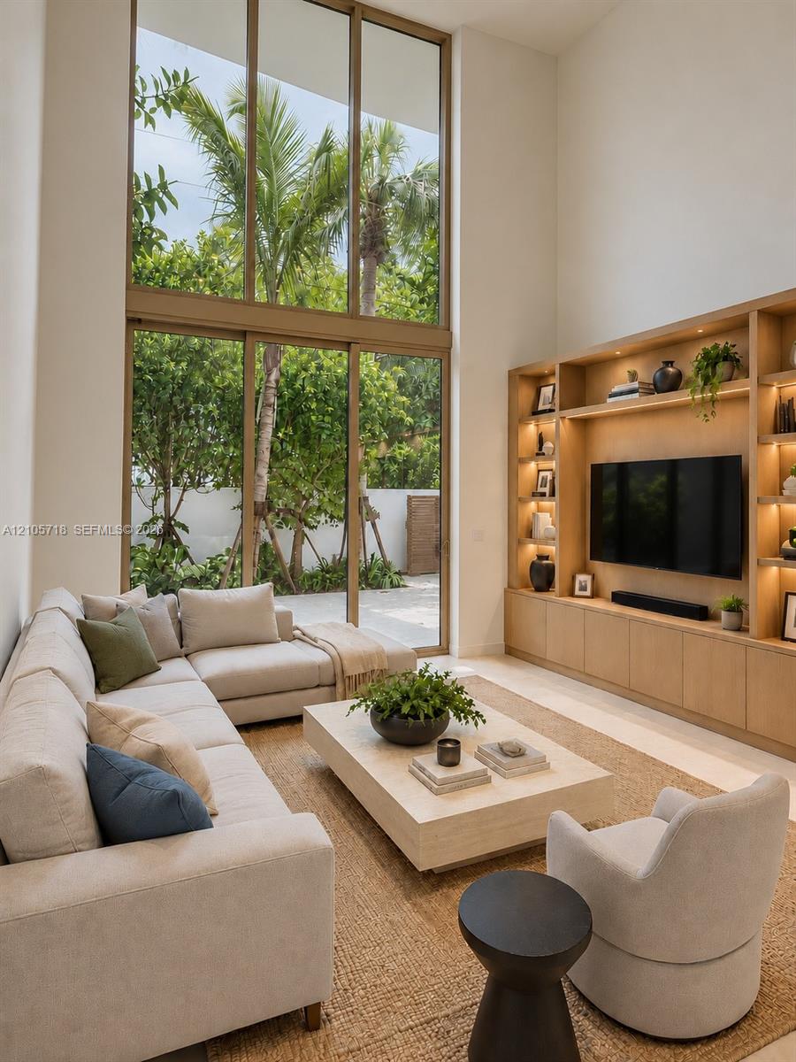 Double-height ceiling featuring floor-to-ceiling windows, custom built-in wood cabinetry with integrated lighting, and neutral stone flooring