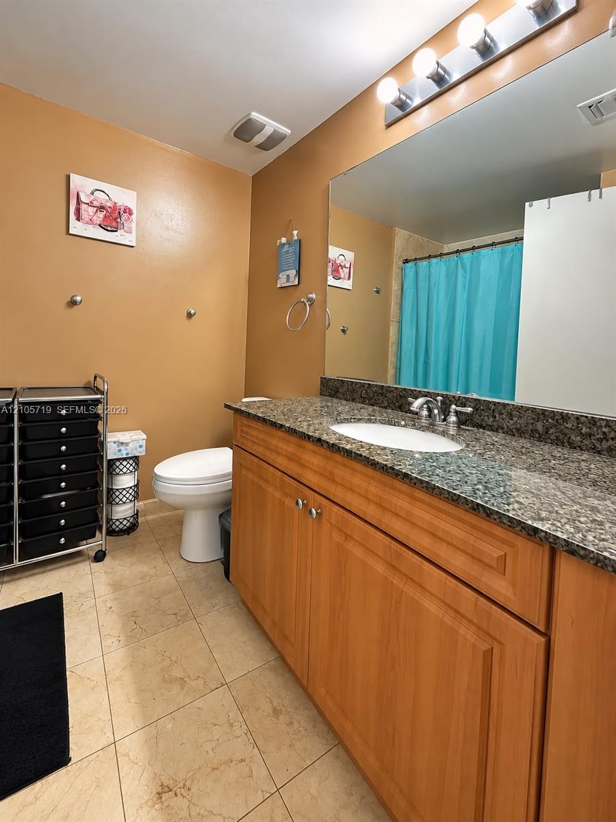 Bathroom featuring a wood-finish vanity with a stone-composite countertop, undermount sink, expansive wall-mounted mirror, and tile flooring