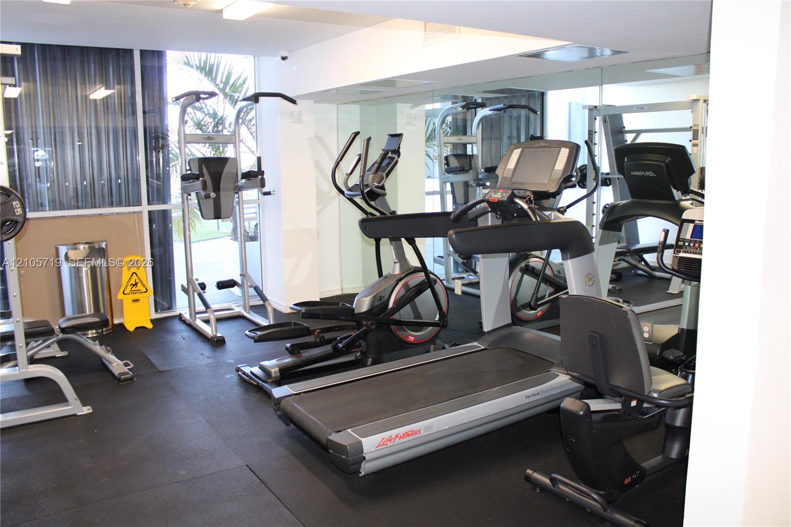 Fitness center featuring rubber flooring, floor-to-ceiling mirrored walls, and floor-to-ceiling windows