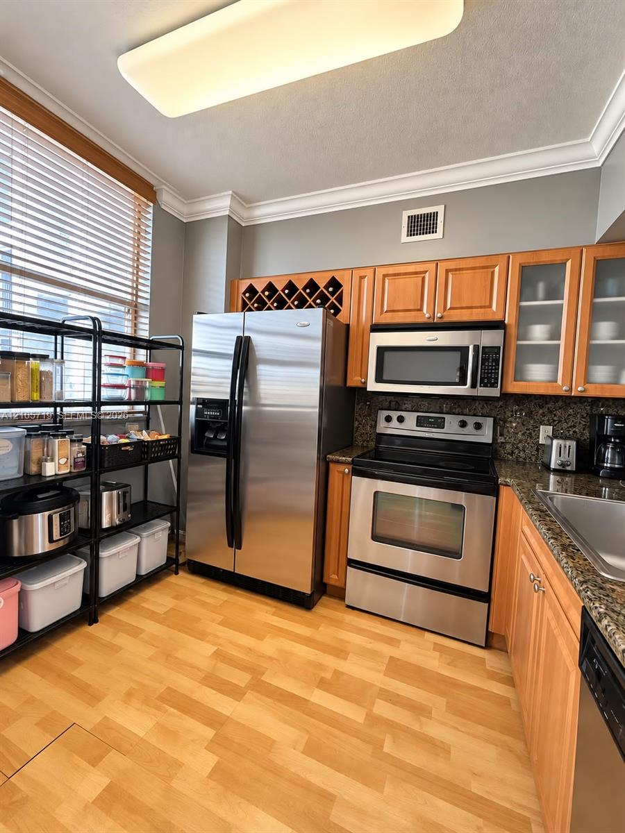 Kitchen featuring wood-finish cabinetry, natural stone countertops, built-in wine storage, stainless steel appliances, and crown molding
